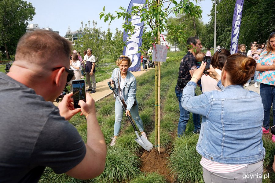 Kobieta z łopatą w ręku podsypująca ziemią Drzewko Życia w Parku Centralnym. Na pierwszym planie osoby robiące zdjęcia telefonami komórkowymi