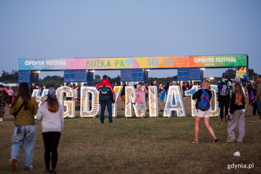 Ludzie podczas festivalu Open'er w Gdyni idący w kierunku bram wyjściowych. Dobrze widoczne napisy "Gdynia 100" i "Bużka, pa".
