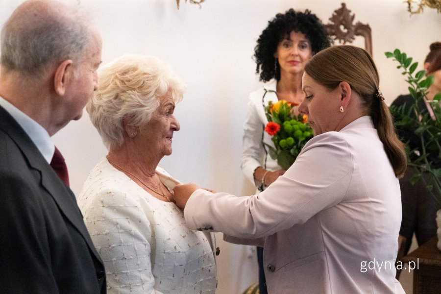 Prezydent wręcza medal kobiecie w białej marynarce