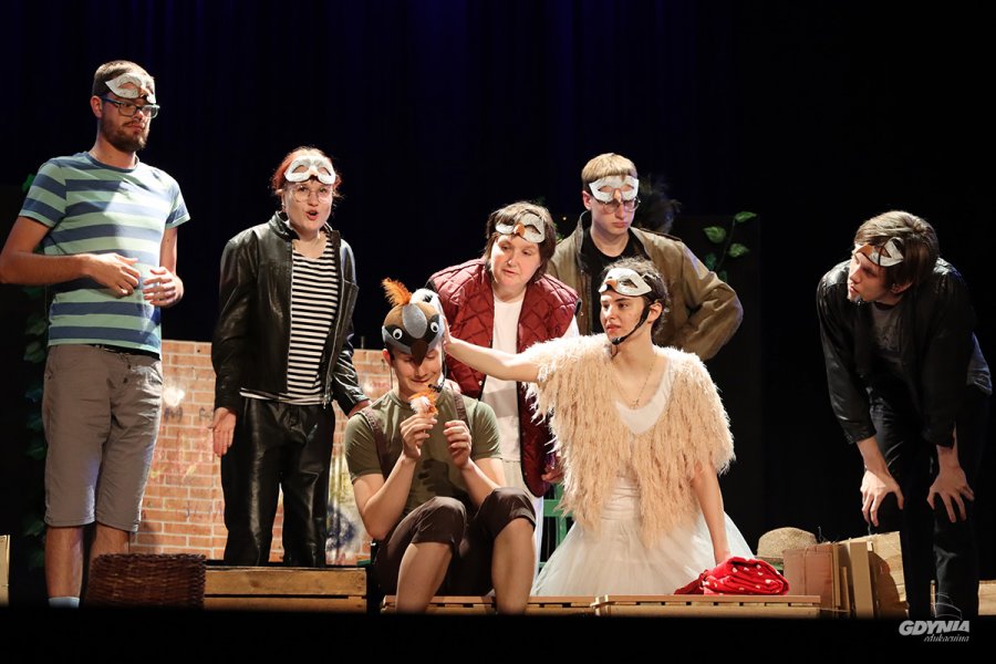 Grupa młodziezy na scenie teatru w przebraniach gołębi.