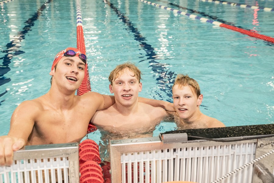 Trzech zawodników w wodzie, przy brzegu basenu