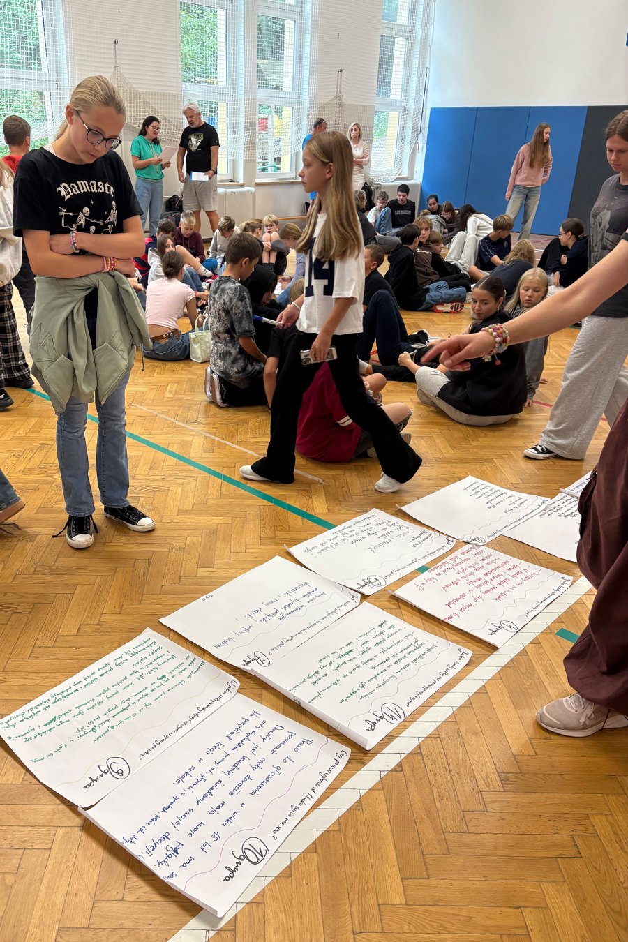 Młodzież stojąca nad pracami na podłodze w trakcie  debaty poświęconej edukacji obywatelskiej