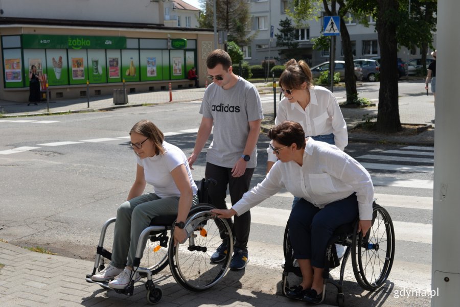 Ludzie na wózkach inwalidzkich przejeżdżają przez przejście dla pieszych.