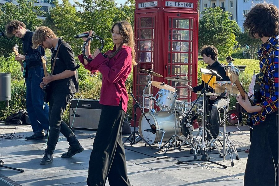 Grupa młodych ludzi grających na instrumentach, w pierwszym planie dziewczyna z tamburynem i chłopak z gitarą, w tle perkusita i dwóch gitarzystów w Parku Centralnym w Gdyni.