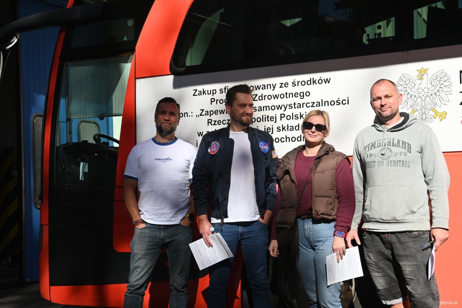 Trzech mężczyn i kobieta na tle ambulansu do pobierania krwi