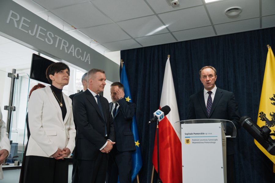 Mężczyzna na m&oacute;wnicy w garniturze, obok flagi: polski i kaszubska