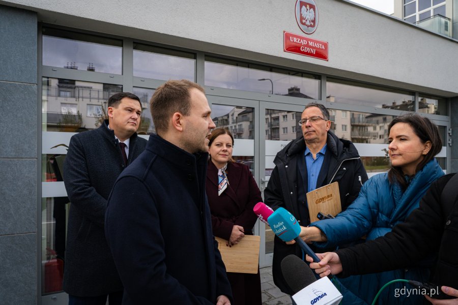Od lewej: radny Norbert Anisowicz, sekretarz miasta Łukasz Kobus, prezydent Gdyni Aleksandra Kosiorek, rzecznik prasowy Urzędu Miasta Gdyni Tomasz Złotoś i przedstawiciele mediów przed nowo otwartym Punktem Obsługi Mieszkańców Urzędu Miasta Gdyni na Chwarznie-Wiczlinie, w lokalu przy ul. Tęczowej 37 (fot. Kamil Złoch)