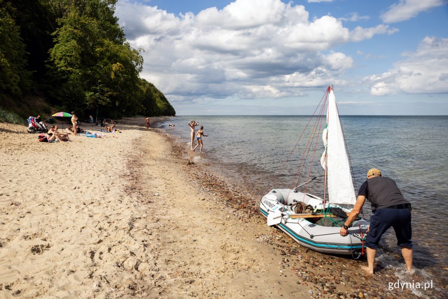 Ludzie plażują na plaży, mężczyzna szykuje na brzegu łódź.