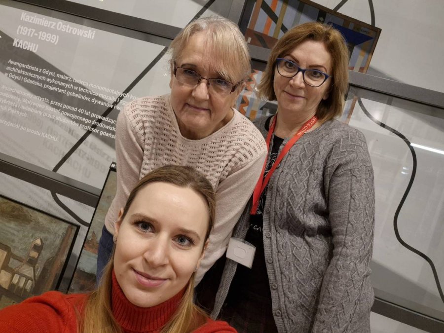 Kobiety w jasnym pomieszczeniu na tle szarej tablicy informacyjnej