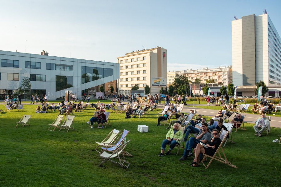 Uczestnicy festiwalu SLOT Pomorze siedzą na leżakach rozstawionych na trawniku na placu Grunwaldzkim. w tle budynek Gdyńskiego Centrum Filmowego i hotelu Mercure // fot. Anna Rezulak
