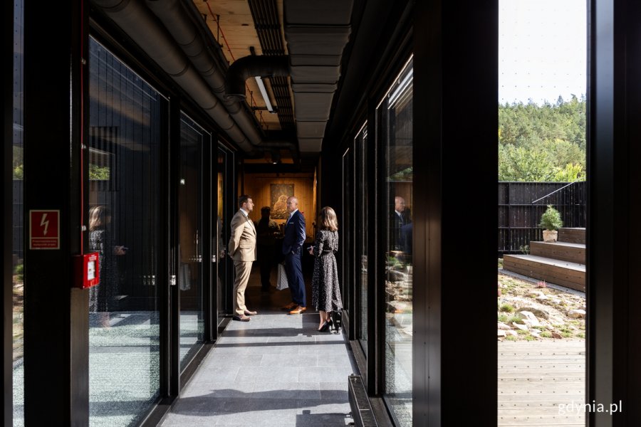 Ludzie stoją w przeszklonym korytarzu drewnianego nowoczesnego budynku.