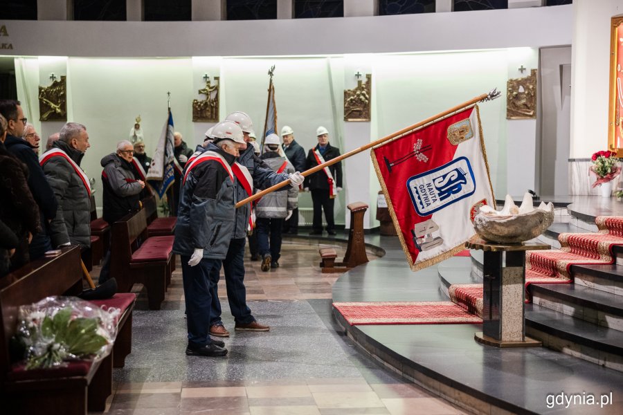 Mężczyźni stojący w kościele i pochylający sztandar w kierunku ołtarza