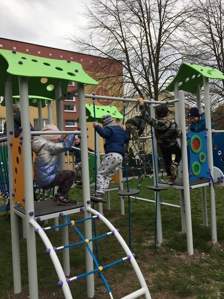 Dzieci bawią się na zabawce, przechodzą po krążkach zawieszonych pionowo na linach.
