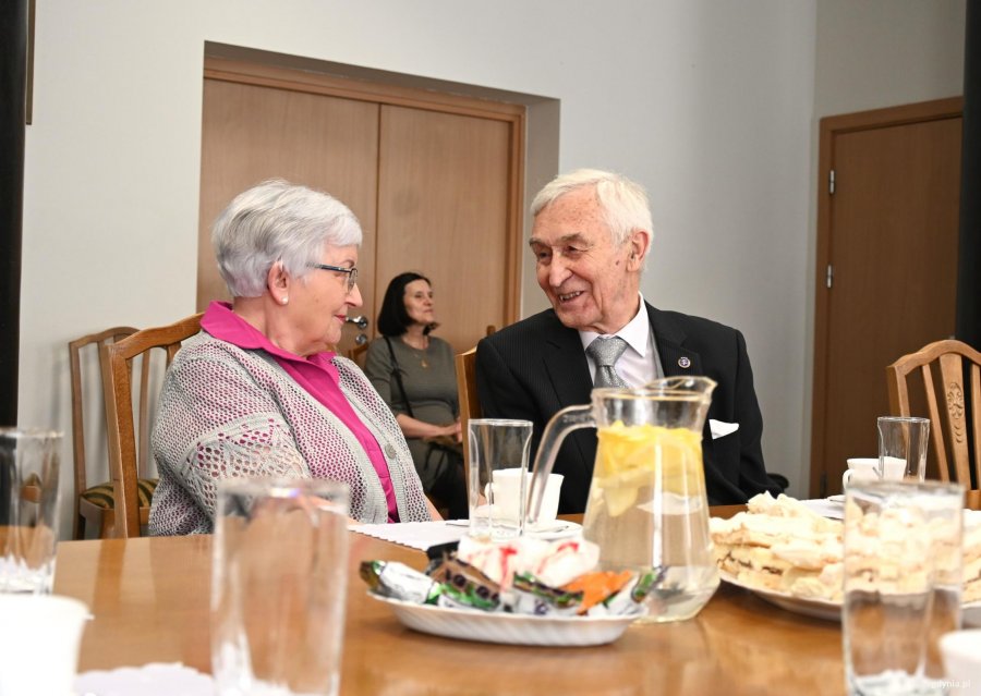 Starsi państwo przy stole uśmiechają się do siebie