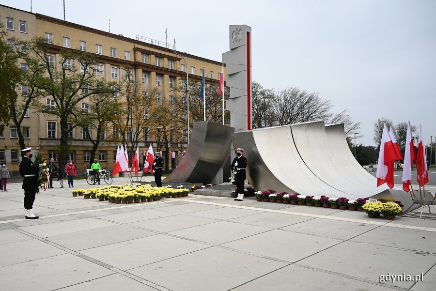 Oficjalne uroczystości z okazji Święta Niepodległości odbyły się przy pomniku Polski Morskiej. Przed pomnikiem stoi posterunek honorowy złożony z dwóch marynarzy w galowych mundurach. Po obu stronach pomnika powiewają biało-czerwone flagi. Przed nim ustawione są donice z różnokolorowymi chryzantemami. Przed pomnikiem stoi marynarz z wieńcem // fot. Michał Puszczewicz