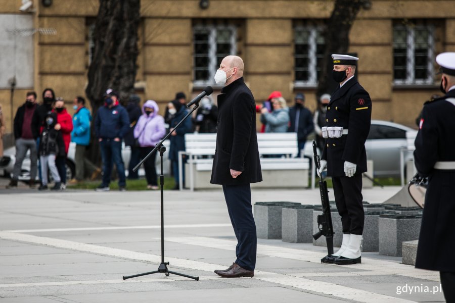 Bartosz Bartoszewicz - wiceprezydent Gdyni wygłasza okolicznościowe przemówienie z okazji Dnia Flagi RP. Z nim stoi posterunek honorowy Marynarki Wojennej. W tle mieszkańcy uczestniczący w uroczystości // fot. Karol Stańczak