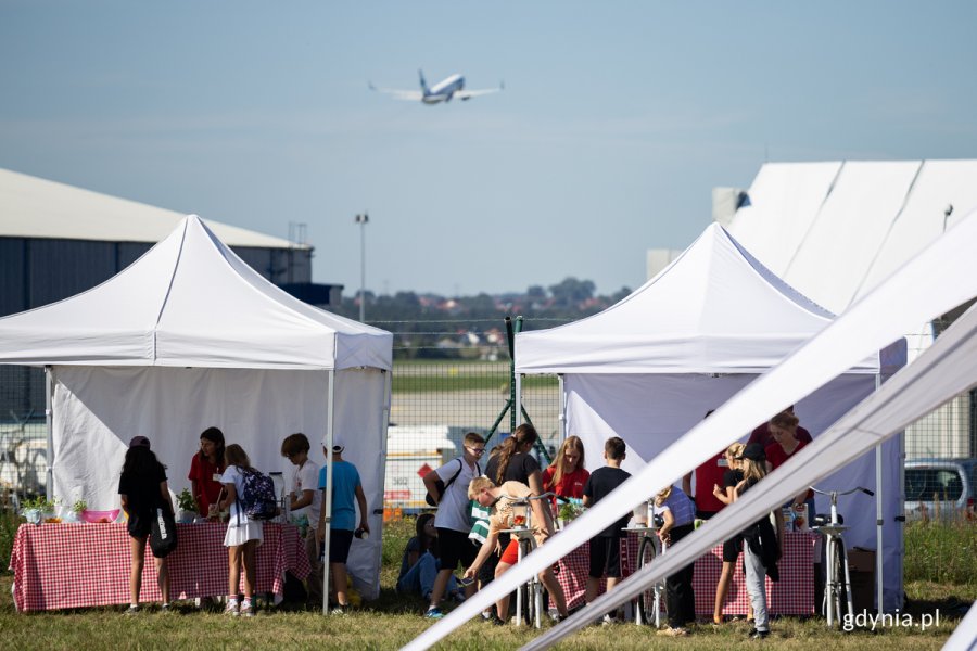Namioty z jedzeniem i piciem na pikniku na lotnisku, w tle leci samolot.