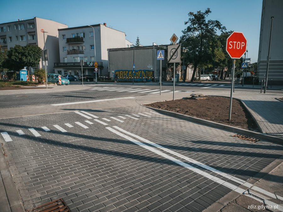 chodniki, wyniesione skrzyżowanie z kostki oraz przejścia dla pieszych po przebudowie. Widoczne oznakowanie, w tle budynki i tereny zielone