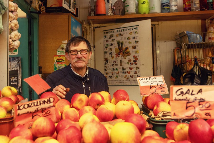 Sprzedawca na hali targowej widziany zza stosu jabłek.