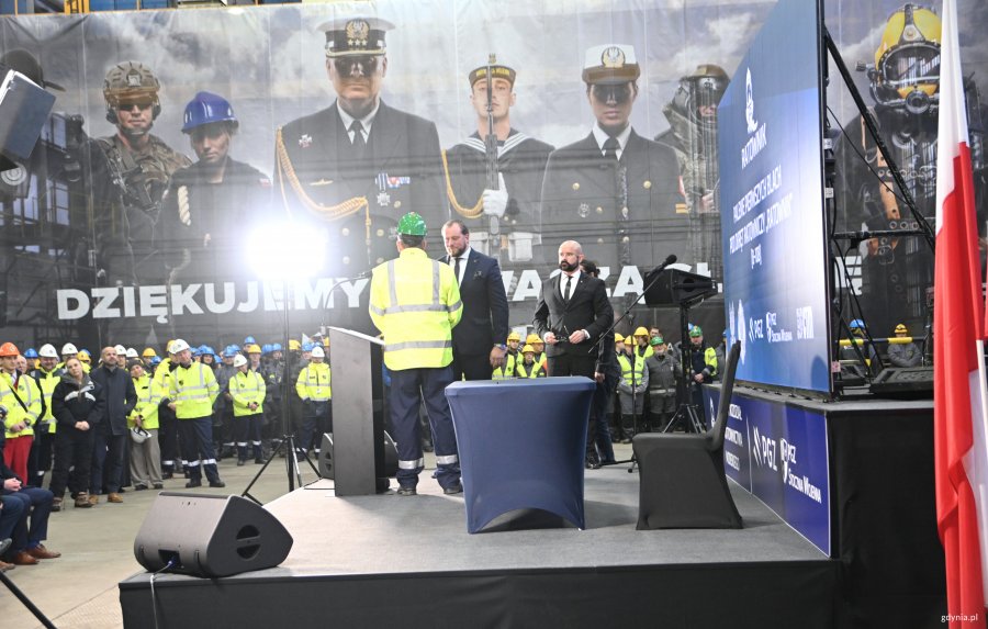 Dwóch mężczyzn: jeden w garniturze, drugi w stroju roboczym na scenie 