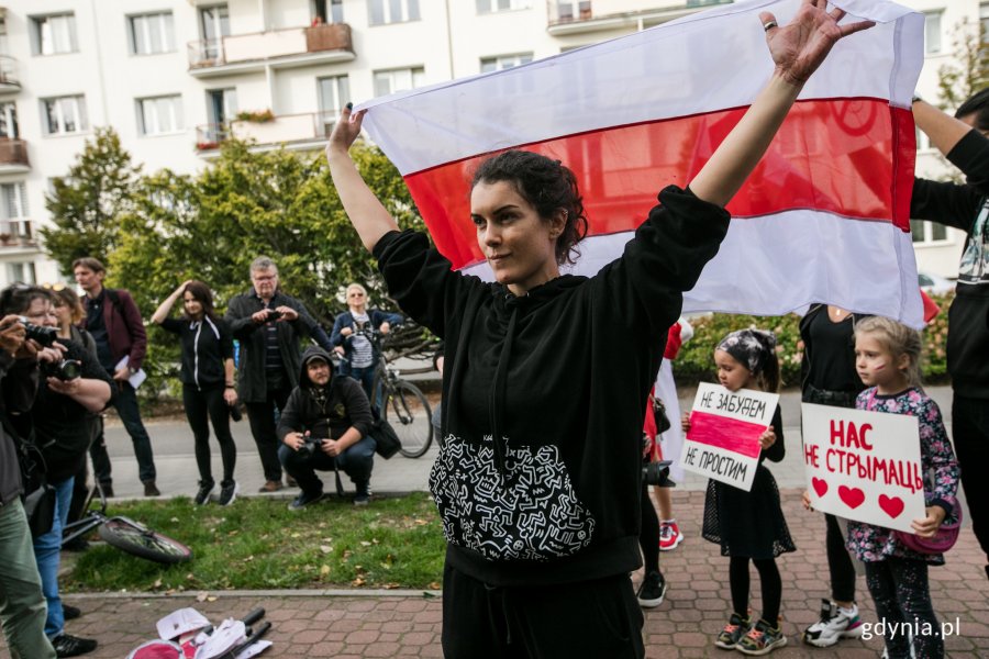 Uczestniczka akcji "Stop przeciwko przemocy wobec narodu Białorusi", ubrana na czarno, z rękoma podniesionymi do góry trzyma białoruska flagę // fot. Karol Stańczak