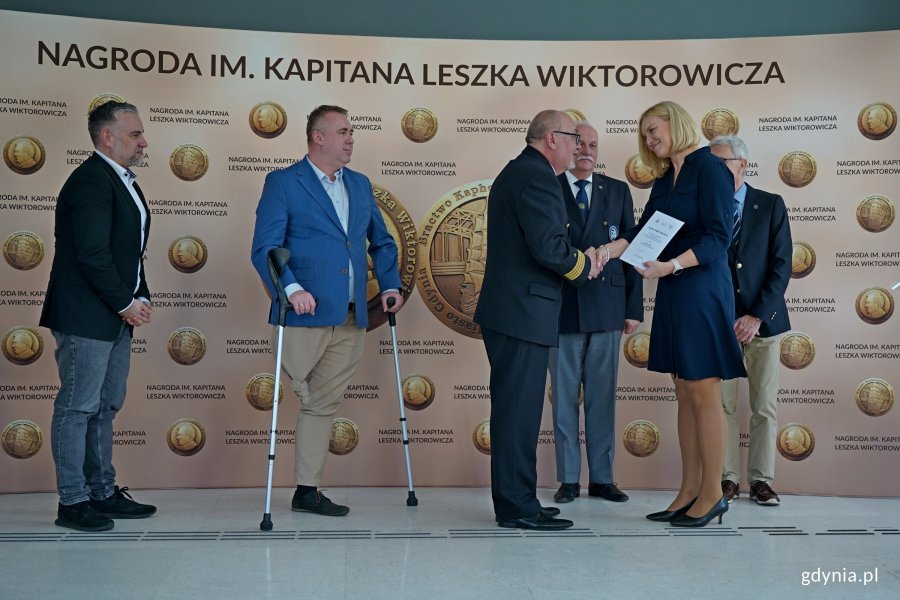 kpt. ż. w. Mariusz Wiktorowicz wręcza Nagrodę im. Kapitana Leszka Wiktorowicza kpt. Magdzie Makowskiej.  Za nimi (od lewej): Paweł Brutel - dyrektor Gdyńskiego Centrum Sportu i członek kapituły, radny Gdyni i członek kapituły Arkadiusz Dzierżyński, kpt. Marek Padjas z Bractwa Kaphornowc&oacute;w i Waldemar Heflich z Press Clubu Polska