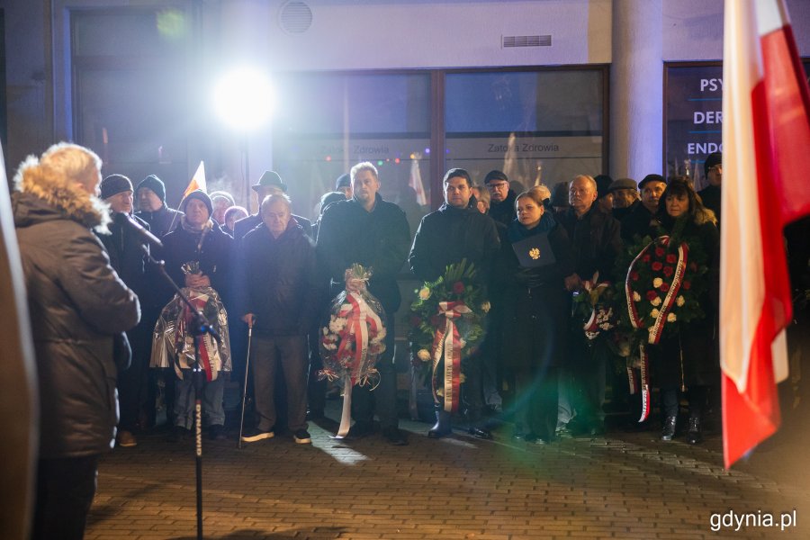 Grupa osób stojących przed pomnikiem i trzymających kwiaty