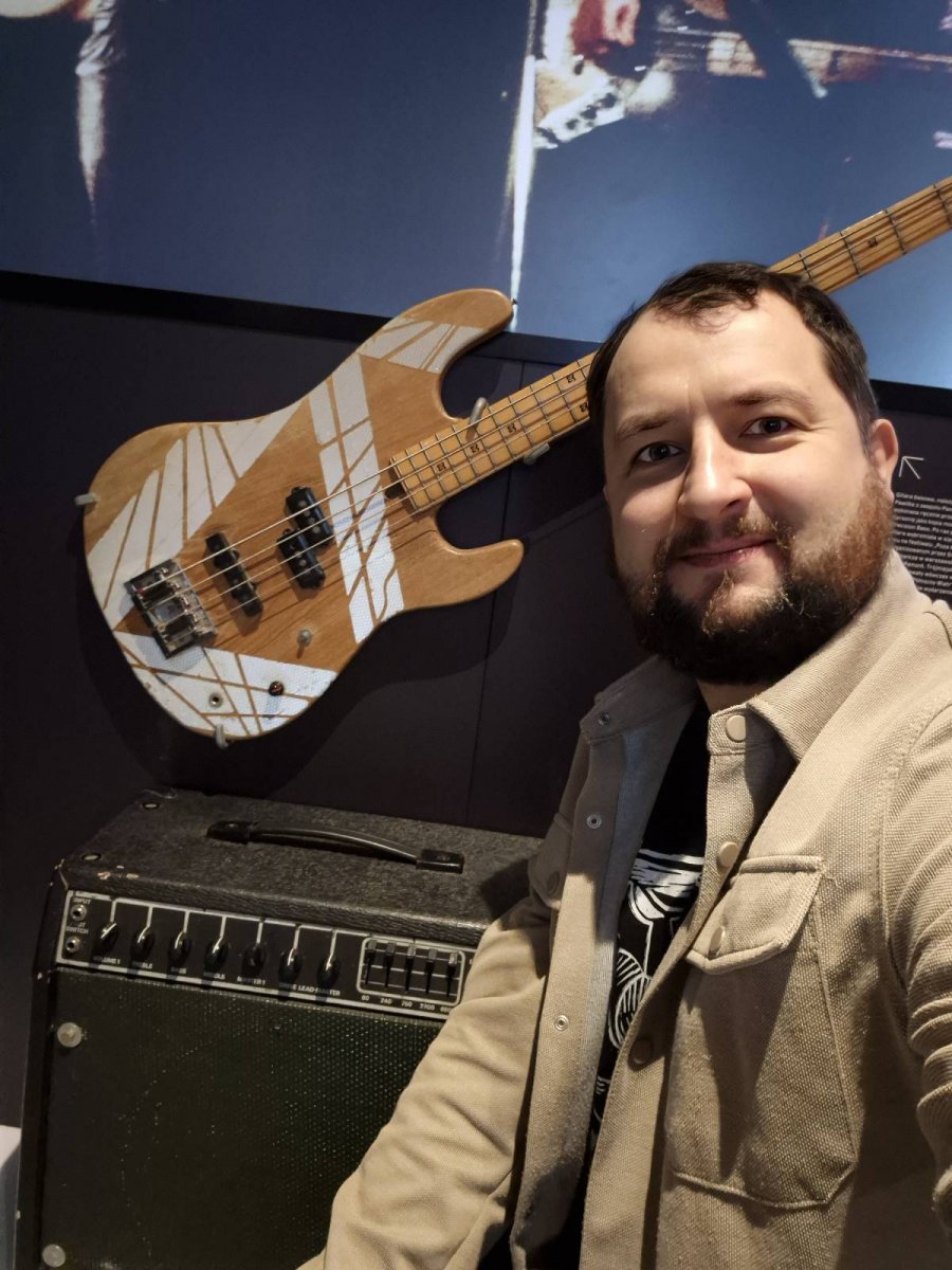 Mężczyzna na tle ściany, do której przymocowana jest brązowo-biała gitara