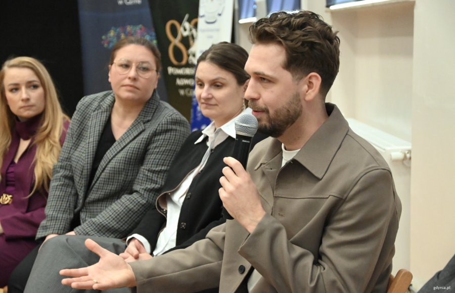 Mężczyzna z mikrofonem, w tle kobiety