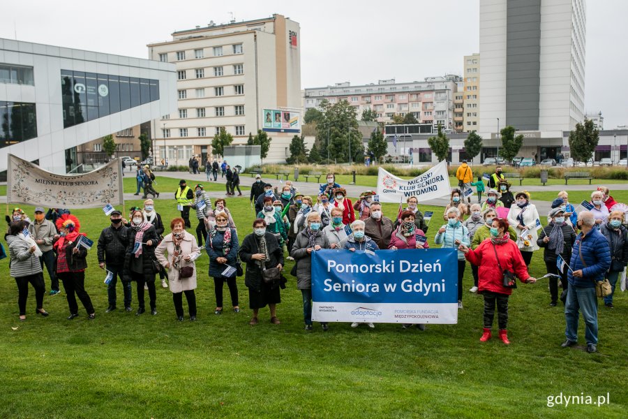 Wielobarwny Pomorski Przemarsz Seniorów ulicami Gdyni. Seniorzy stoją z transparentami na Placu Grunwaldzkim. Fot. Karol Stańczak