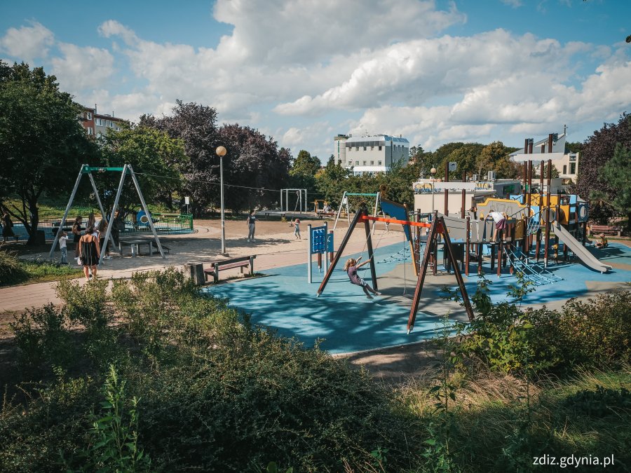 urządzenia zabawowe na niebieskiej nawierzchni, plac zabaw, w tle zieleń