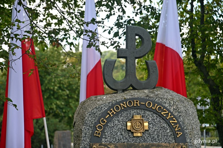 Symbol Polski Walczącej oraz napis "Bóg - honor - ojczyzna" na pomniku Armii Krajowej na skwerze Kościuszki. W tle gałęzie drzew oraz biało-czerwone flagi // fot. Magdalena Czernek