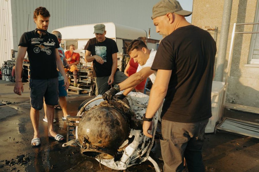 Grupa ludzi stojąca wokół szarego metalowego przedmiotu w kształcie walca