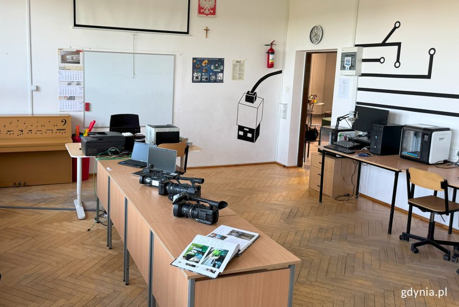 Sala ze stołami, na których stoją kamery video, w dalszym planie radiowęzeł i drzwi wyjściowe z sali