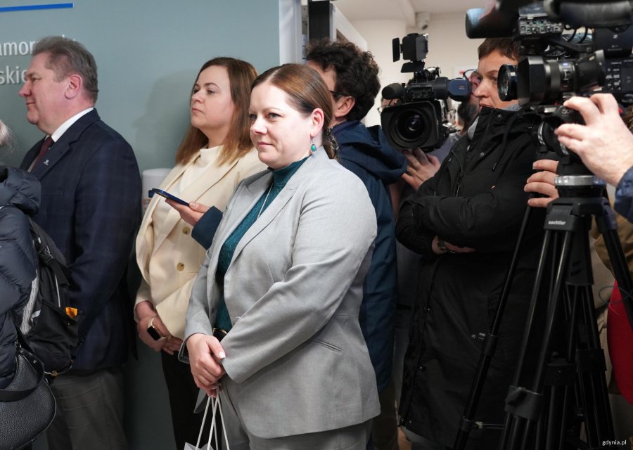 Kobieta w szarej marynarce, za nią kamery