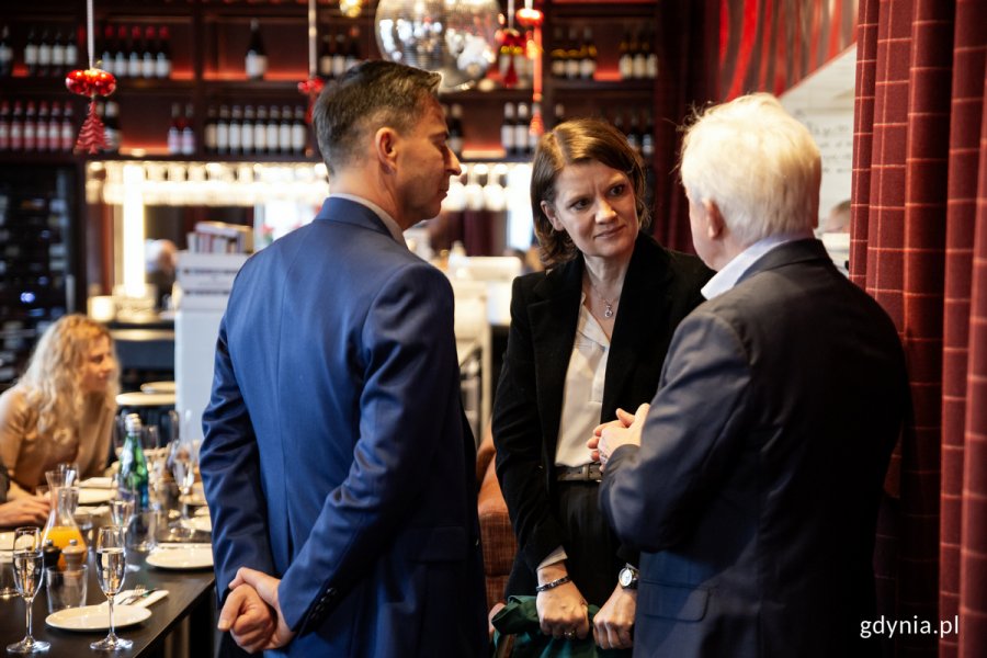 Kobieta i dwóch mężczyzn rozmawiają, stojąc w restauracji.