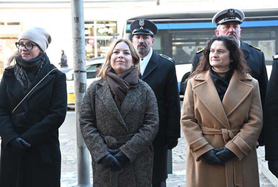 Trzy kobiety w płaszczach, w tle marynarze