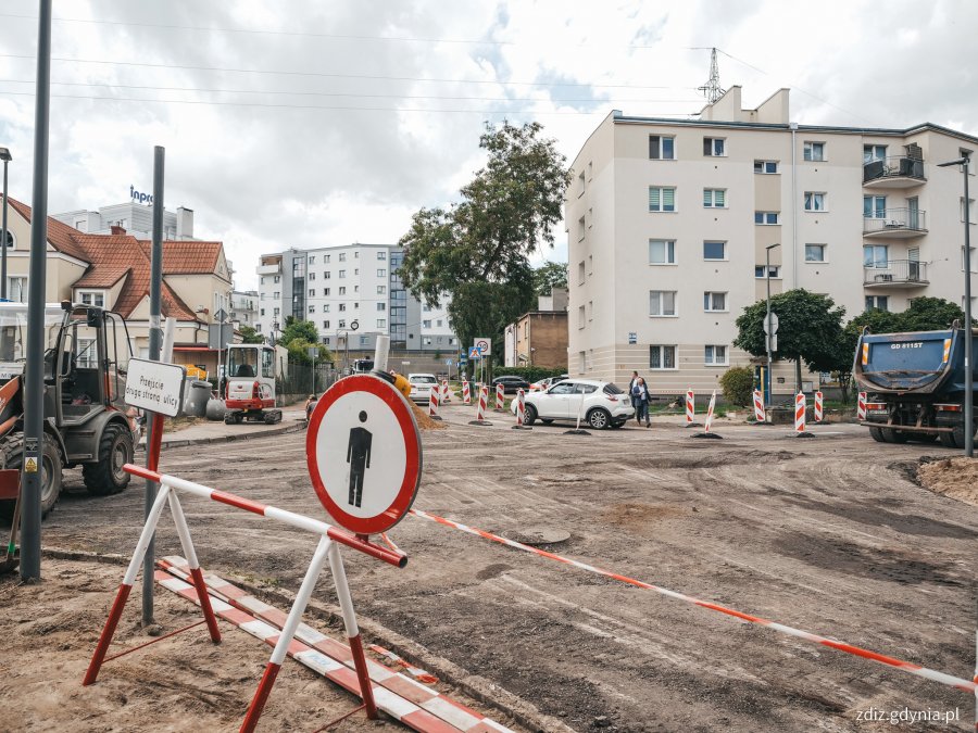 na pierwszym planie oznakowanie "zakaz przejścia", w tle roboty drogowe na skrzyżowaniu, wymiana nawierzchni