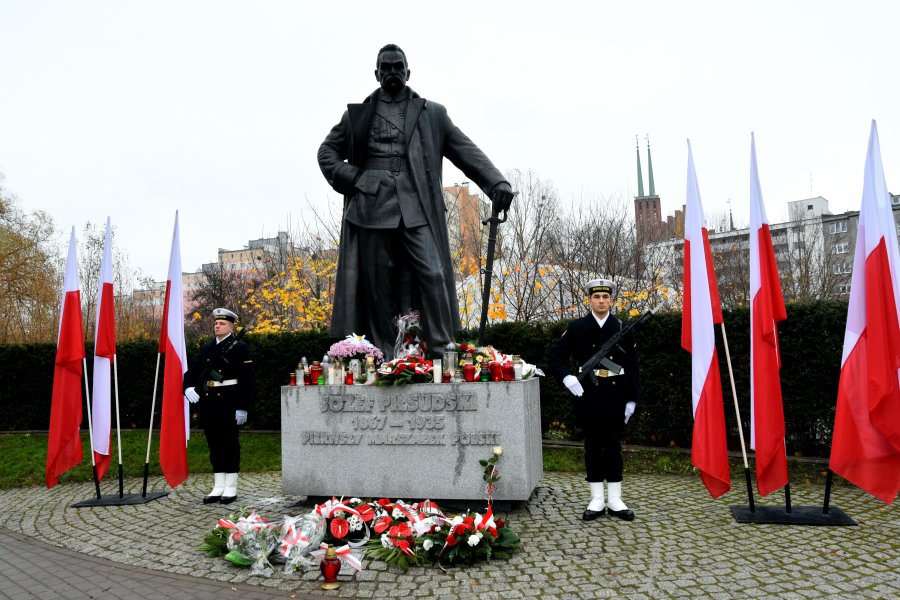 Posterunek honorowy przy pomniku marszałka Józefa Piłsudskiego. Przed pomnikiem leżą wiązanki kwiatów. Obok rząd biało-czerwonych flag // fot. Magdalena Czernek