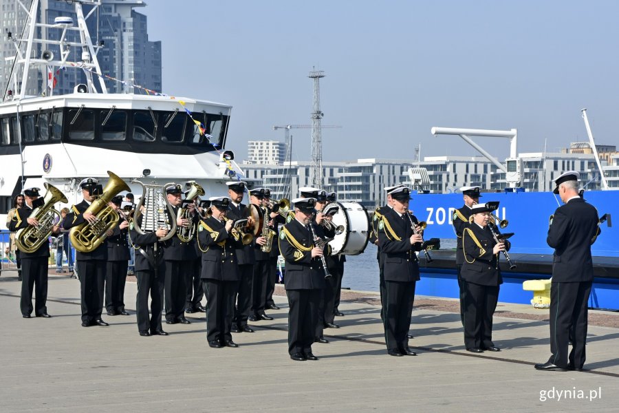 Orkiestra Morskiego Oddziału Straży Granicznej podczas ceremonii chrztu i podniesienia bandery na "Zodiaku II". Grają na róznego rodzaju instumentach, stoją przy burcie statku, za nimi widać napis: "Zodiak II" // fot. Magdalena Czernek