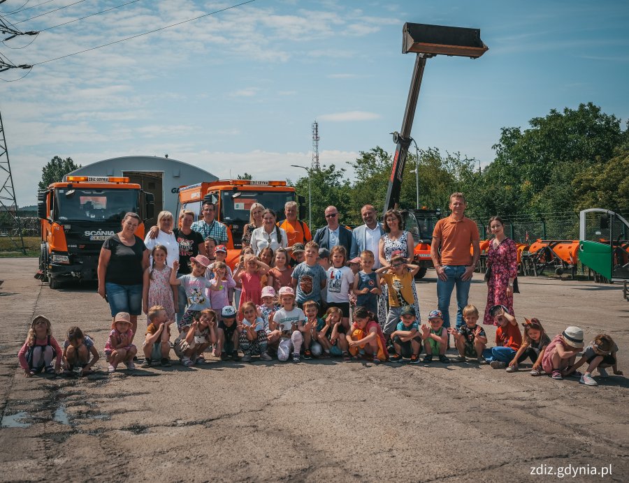 Wizyta przedszkolaków w bazie LIZUD, zdjęcie grupowe, w tle pojazdy do oczyszczania miasta