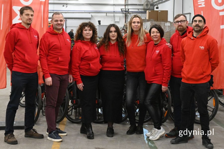 Grupa osób stojących w rzędzie na tle rzędu rowerów