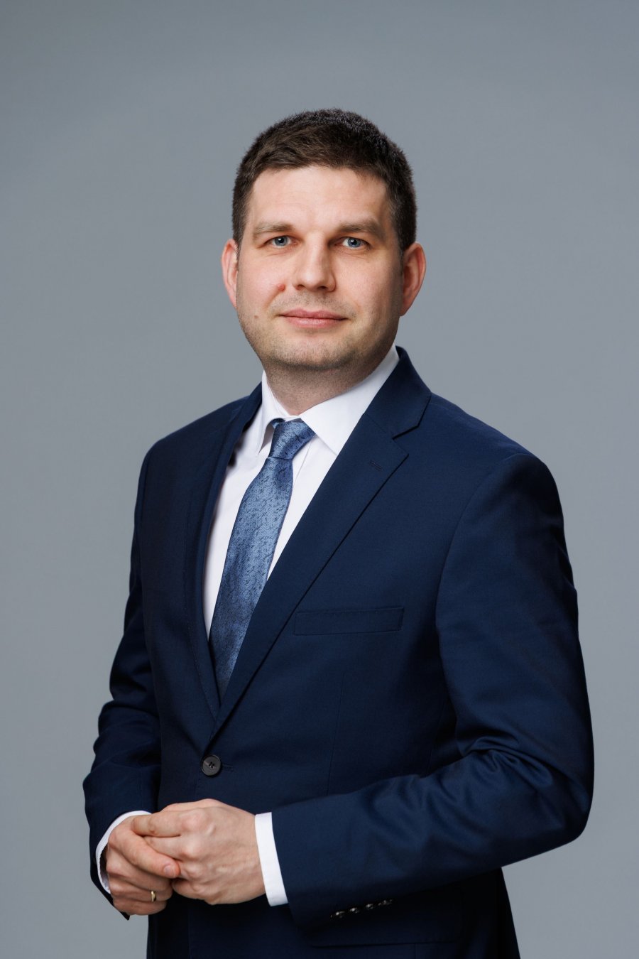 Zdjęcie portertowe: Maciej Zielonka, Wiceprezydent Miasta Gdyni, w garniturze, białej koszuli i krawacie, na szarym tle. 