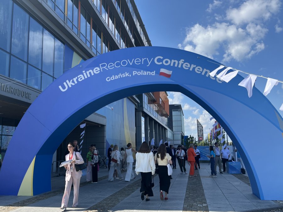 Baner Konferencji Odbudowy Ukrainy (Ukraine Recovery Conference) w Gdańsku  i przechodzący pod nim ludzie