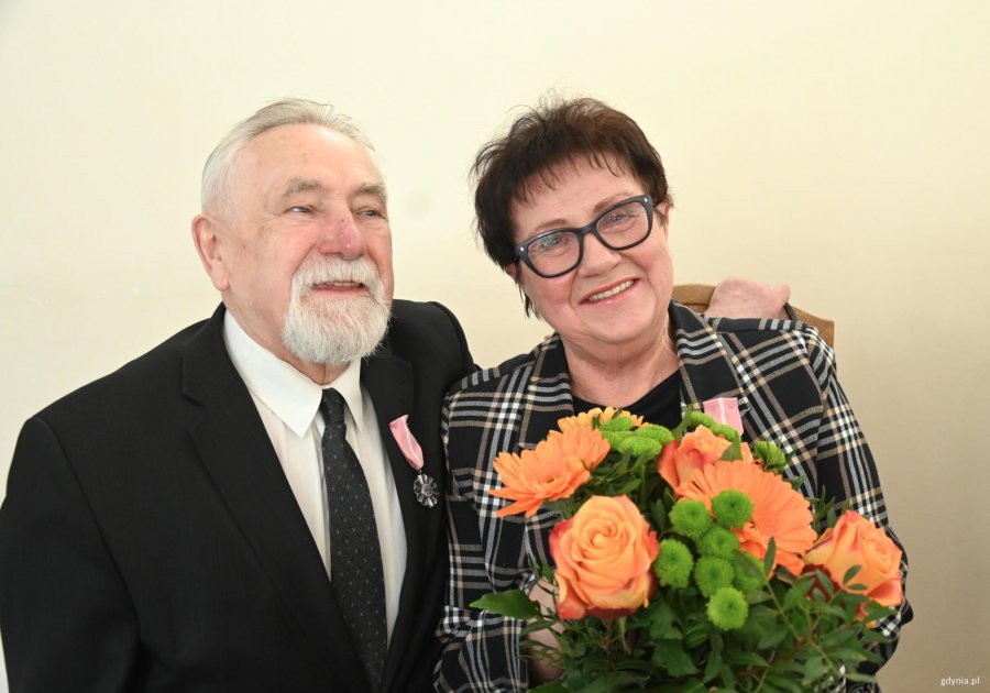 Starszy pan w garniturze, obejmuje kobietę w okularach z bukietem kwiat&oacute;w