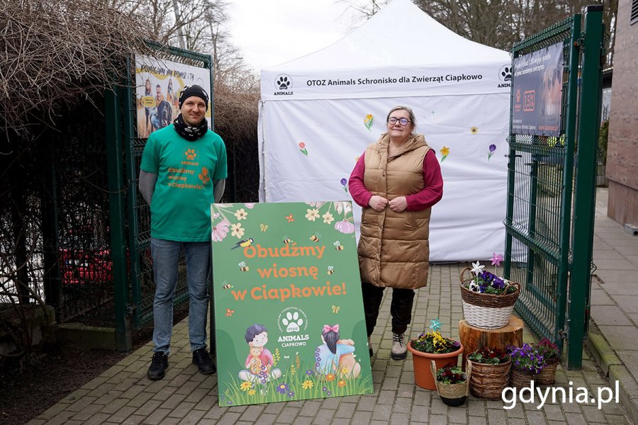 Katarzyna Kownacka - kierownik schroniska OTOZ Animals „Ciapkowo” w Gdyni (po prawej) i Jarosław Florek - zastępca kierownika schroniska OTOZ Animals „Ciapkowo” w Gdyni (po lewej) przed wejściem do schroniska, obok tablicy promującej wydarzenie  „Obudźmy wiosnę w «Ciapkowie»”