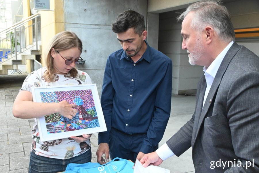 Daria Balabai z Fundacji RC razem z Ihorem Vashchukiem wręczają prezydentowi Wojciechowi Szczurkowi obraz ukraińskiego artysty przedstawiający Chersoń oraz rysunki ukraińskich dzieci