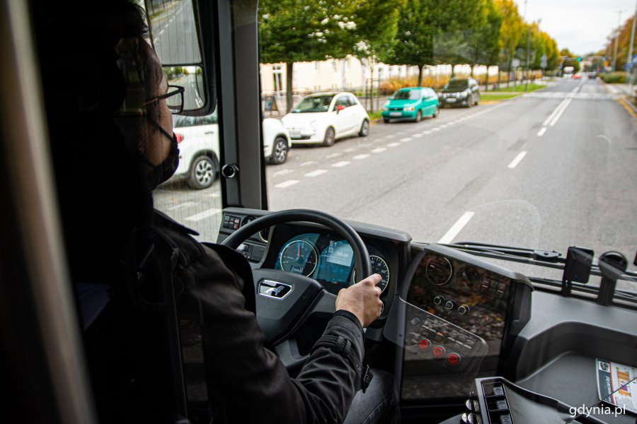 Nowy elektryczny MAN w Gdyni - widok z kabiny kierowcy na ulicę, po lewej stronie stoją zaparkowane samochody. Na pierwszym planie kierowca kierujący autobusem i jego kabina, fot. Kamil Złoch