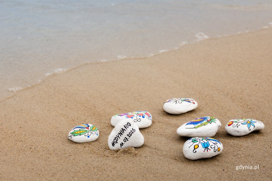 Kamyki malowane w kaszubskie wzory leżą na piasku na plaży