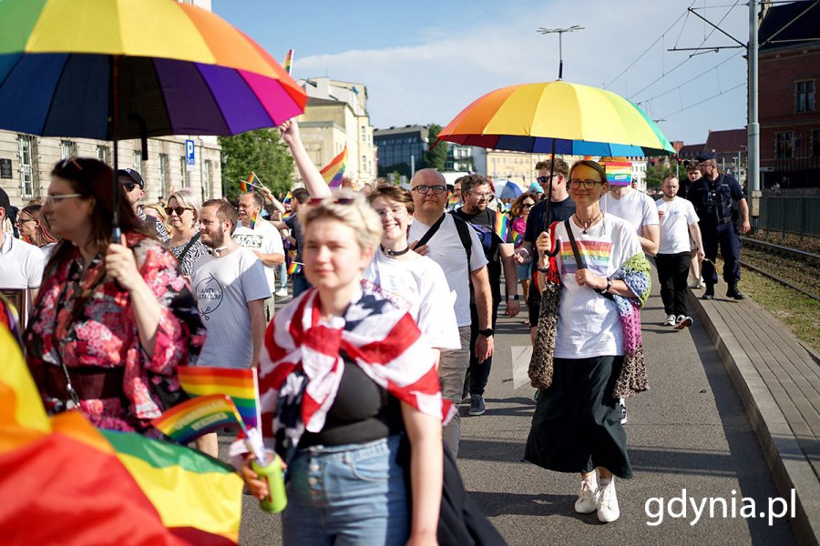 Grupa osób z tęczowymi flagami idąca ulicą